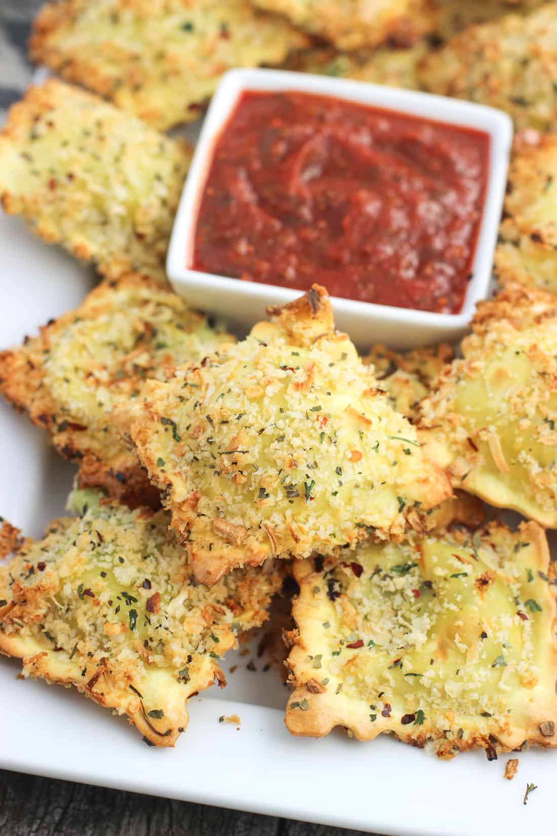 A tray of toasted ravioli with a small bowl of marinara sauce.