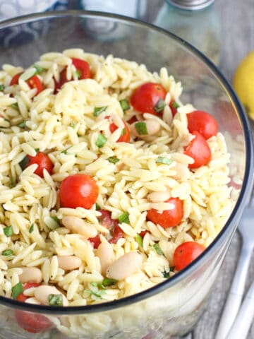 A large glass bowl of orzo pasta salad.
