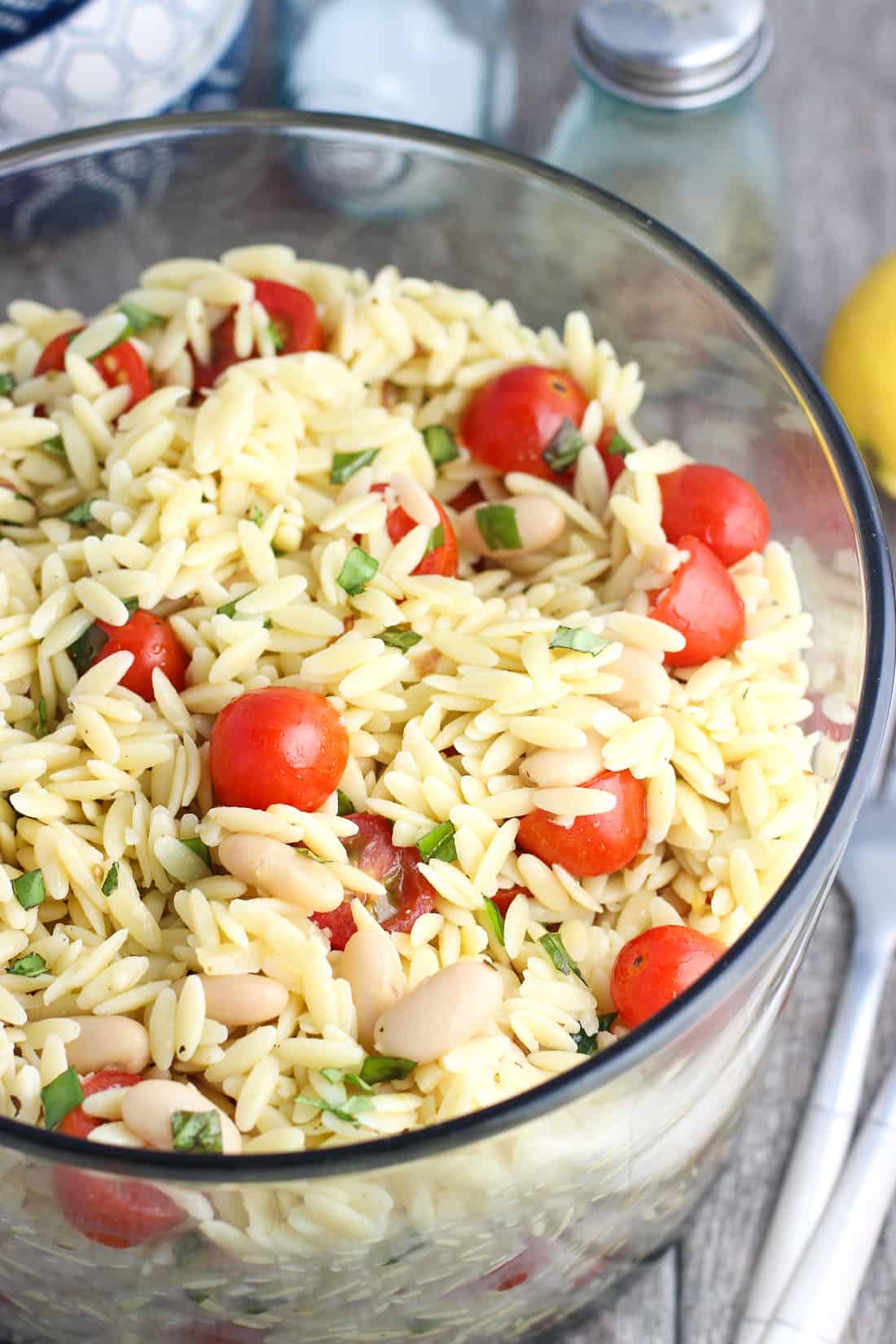 A large glass bowl of orzo pasta salad.