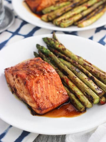 A salmon fillet, sauce, and asparagus on a plate.