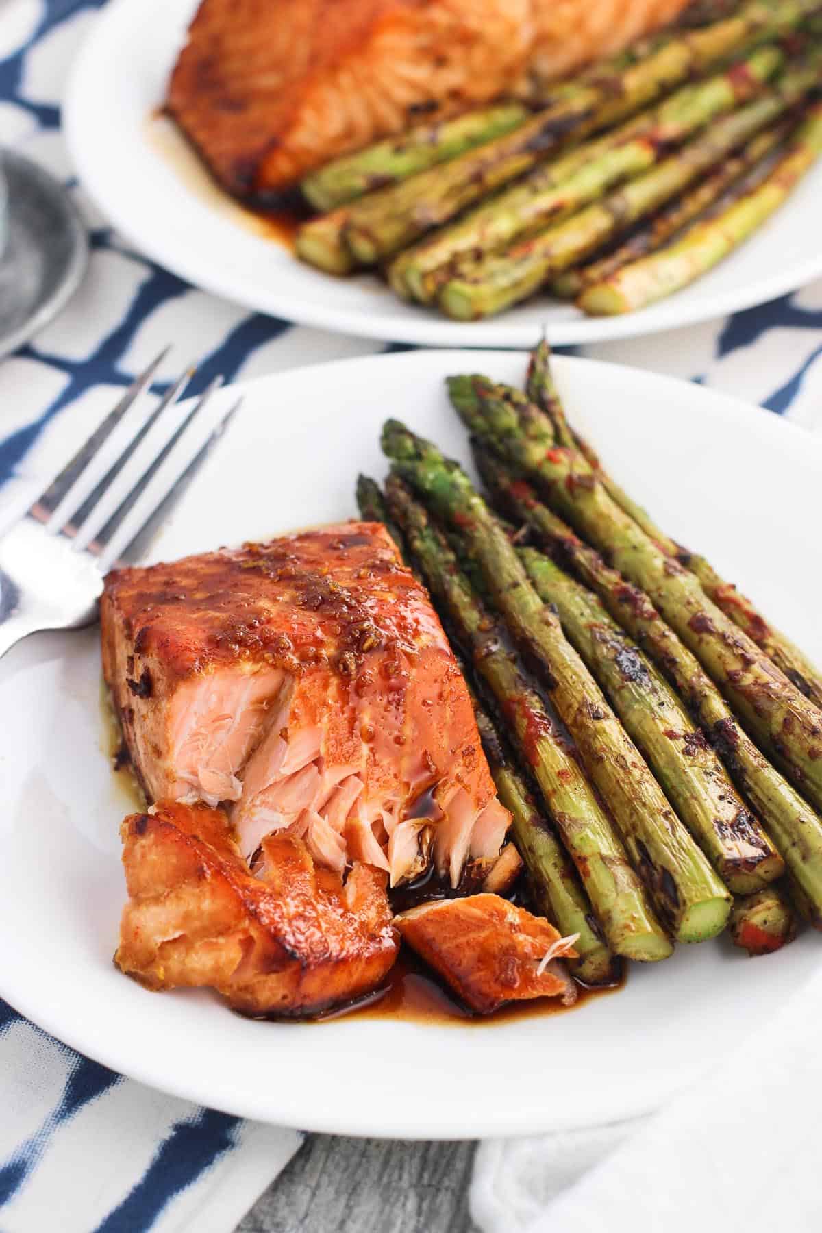 A cooked salmon fillet flaked on a plate with asparagus and sauce.
