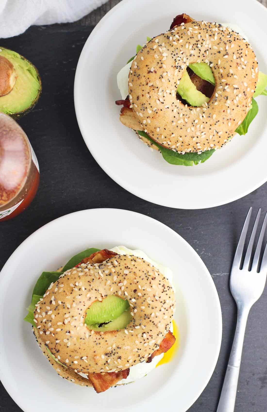 An overhead picture of two breakfast sandwiches on small plates next to a fork and a bottle of hot sauce