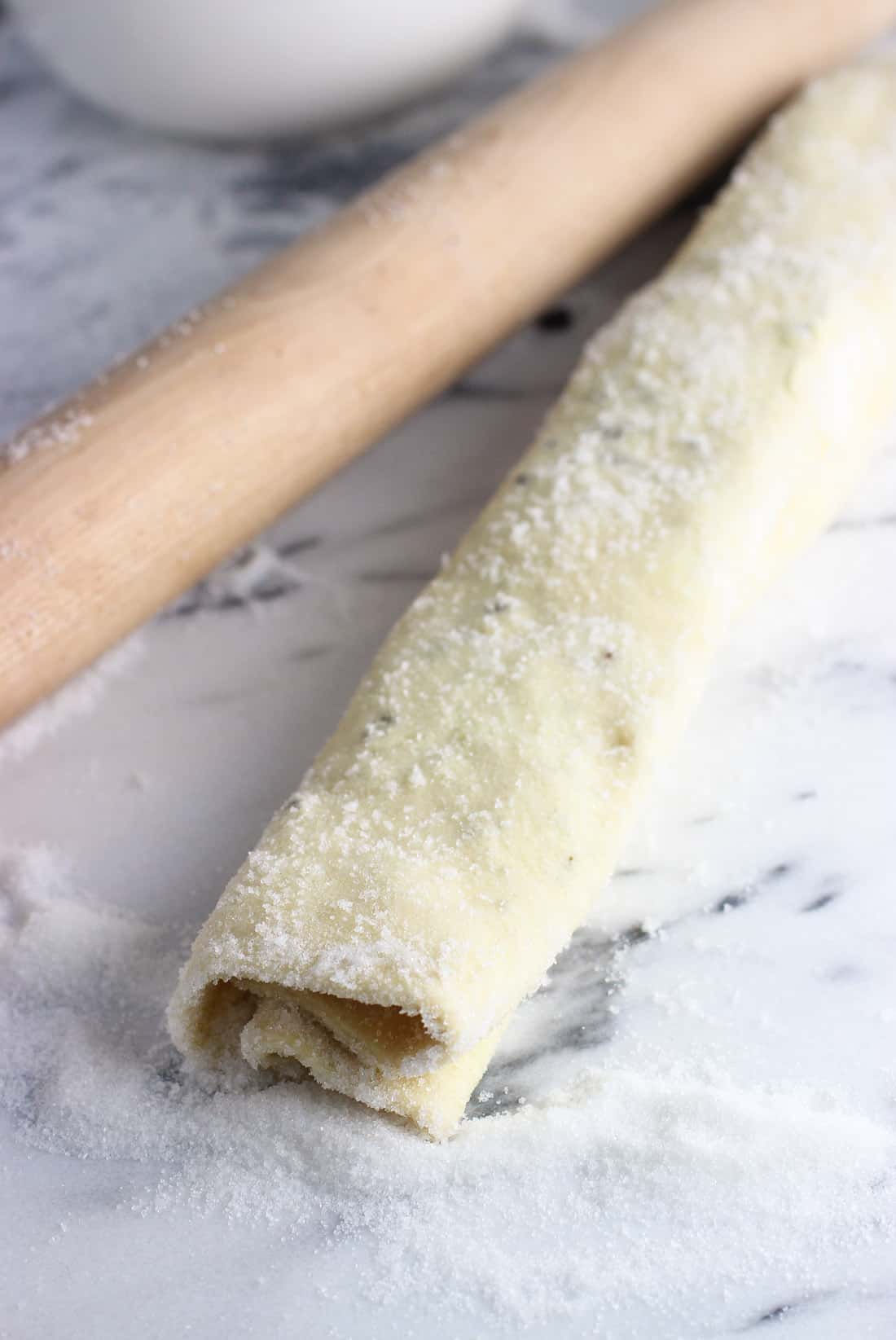 Rolled up puff pastry on a marble board next to a wooden rolling pin