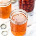 Two snakebite drinks in glass jars with a jar of maraschino cherries in the background