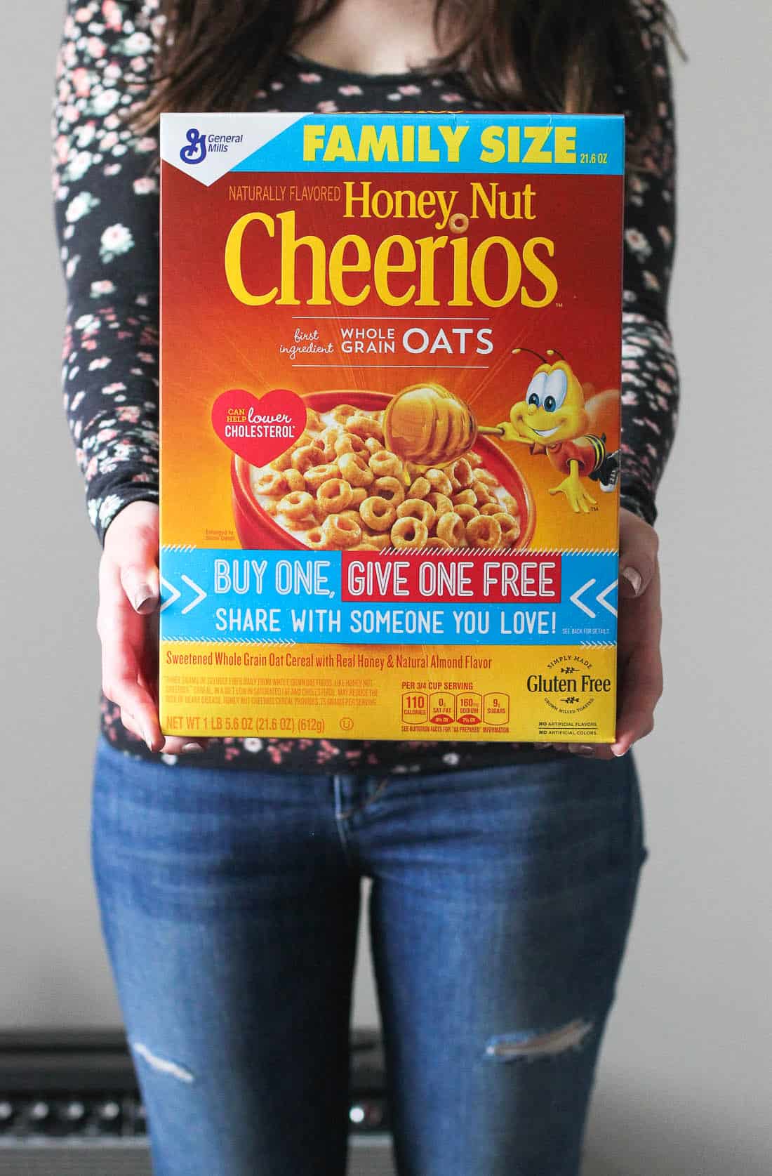 A woman holding a box of family size Honey Nut Cheerios in front of her