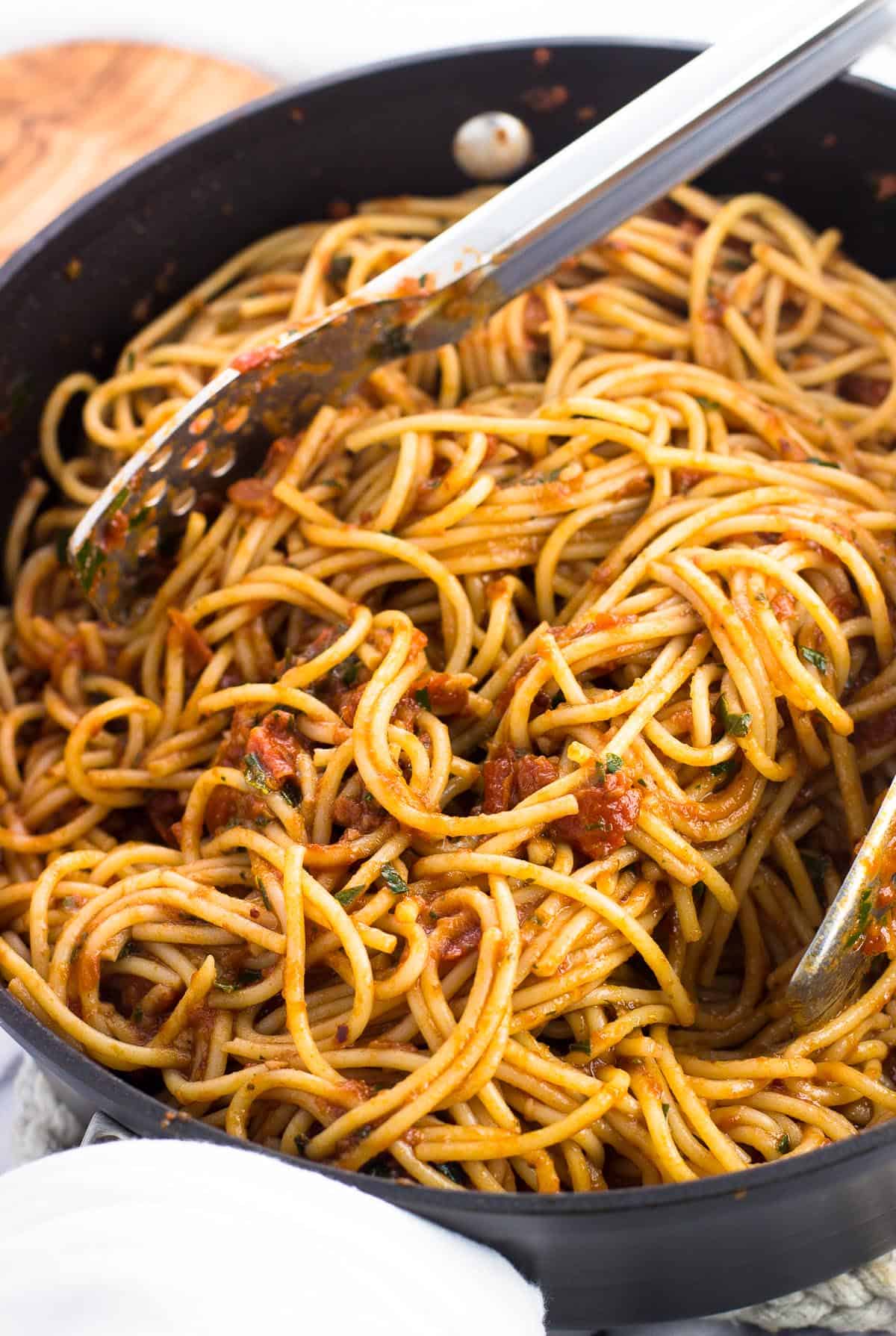 Spaghetti tossed in the sauce in a pan with a pair of tongs.