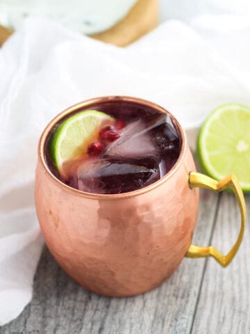 A pomegranate mule in a frosty hammered copper mug with two large square ice cubes, a lime wedge, and pomegranate arils