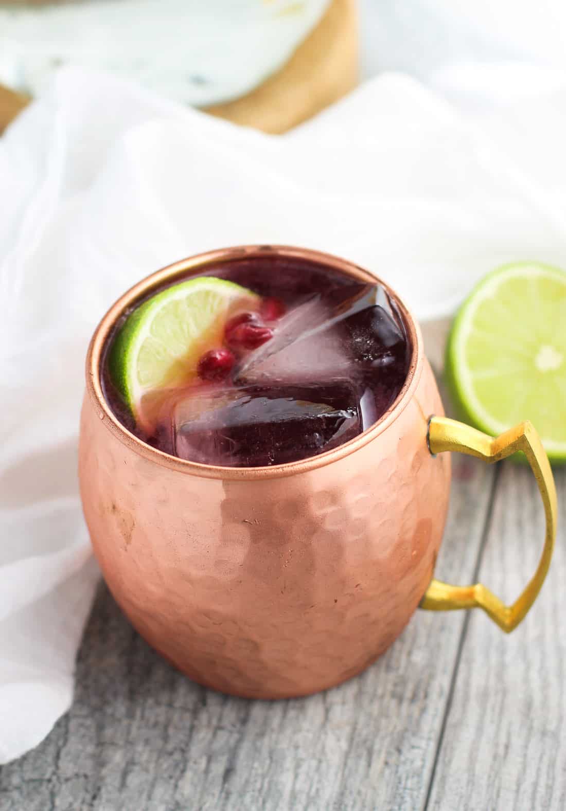 A copper mug filled with a pomegranate Moscow mule served over ice with pomegranate arils and a lime wedge