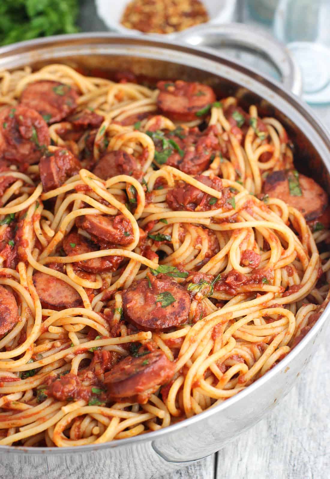 A large metal pan with taller sides filled with spaghetti, smoked sausage, and sauce ready to serve