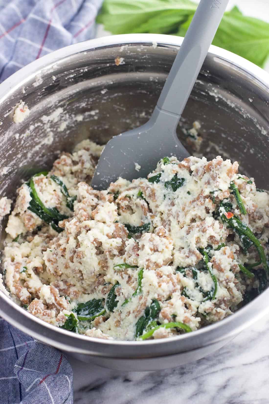 Ricotta and sausage lasagna filling mixed together in a metal mixing bowl with a spatula.