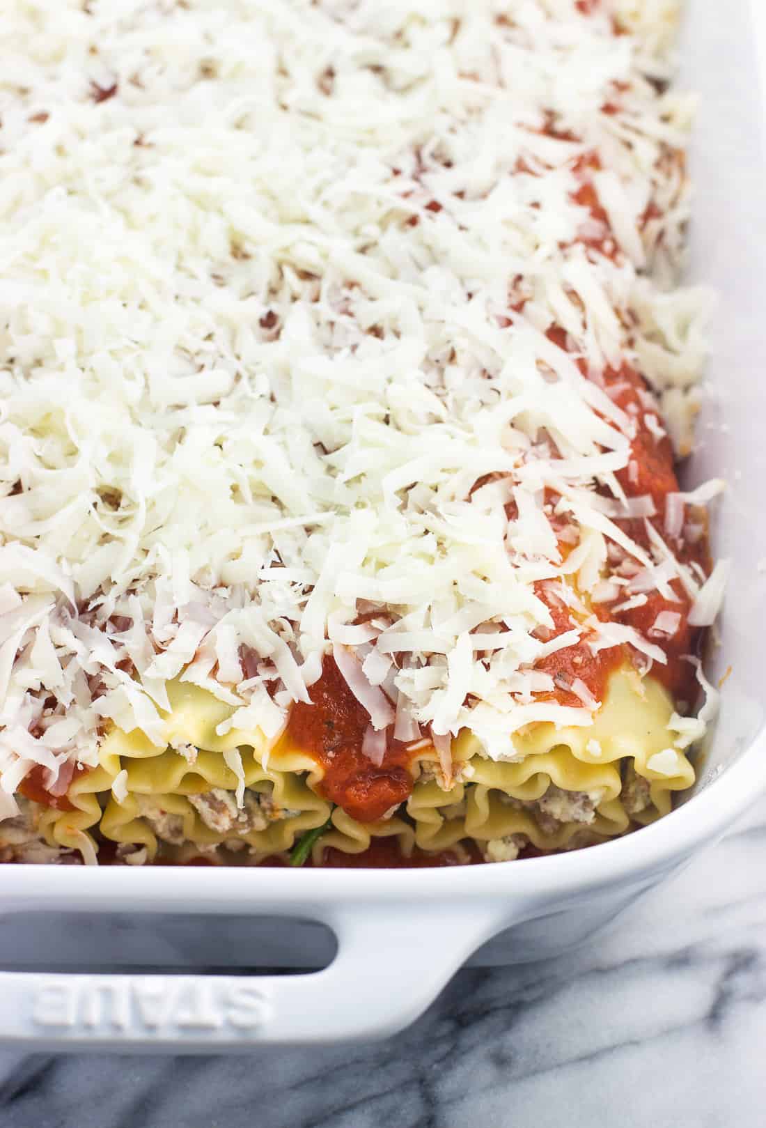 Spinach lasagna rolls in a large ceramic baking dish covered in marinara sauce and shredded mozzarella cheese