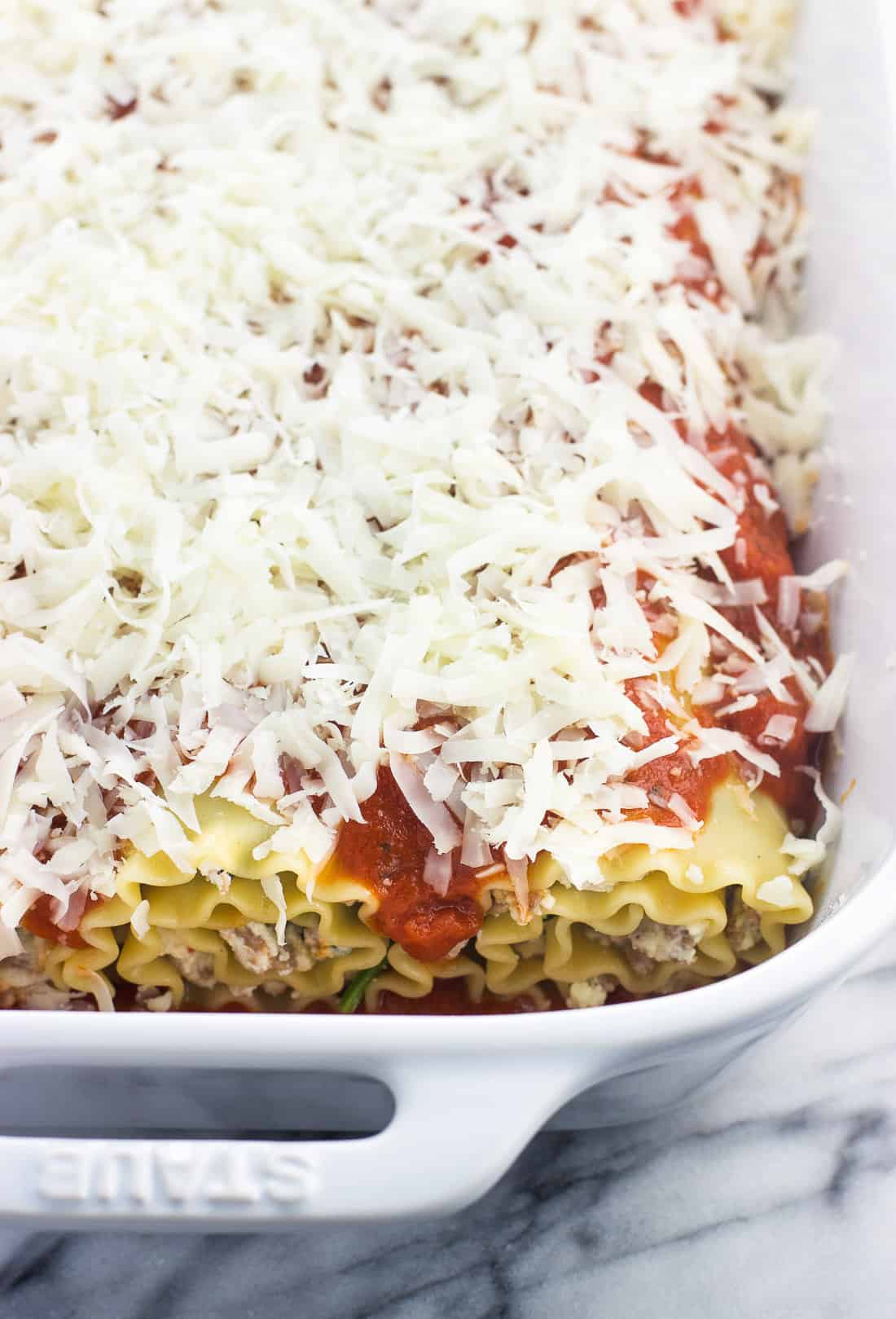 Spinach lasagna rolls in a large ceramic baking dish covered in marinara sauce and shredded mozzarella cheese.
