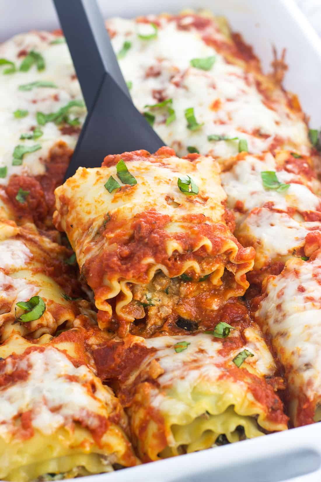 A spatula lifting out a sausage lasagna roll out of the baking dish.
