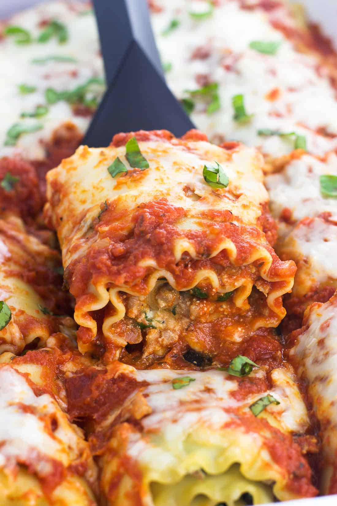 A lasagna roll on a spatula lifting out of a baking dish.