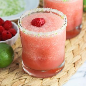 Two frozen blended margaritas garnished with salty lime rims and fresh raspberries.
