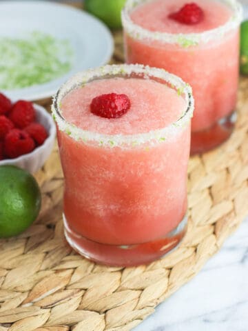 Two frozen blended margaritas garnished with salty lime rims and fresh raspberries.