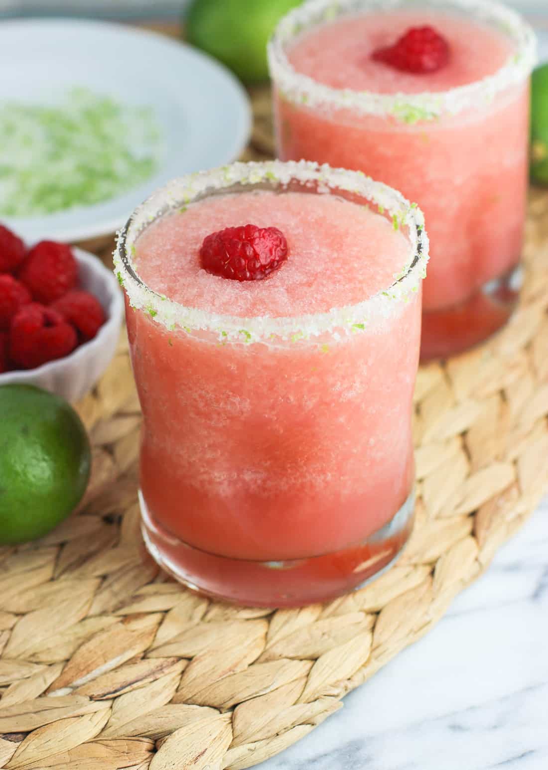 Two frozen blended margaritas garnished with salty lime rims and fresh raspberries.