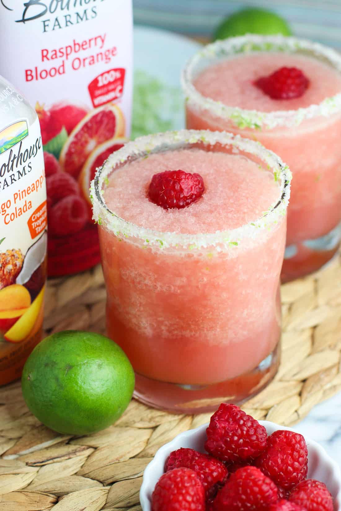 Two frozen cocktails and fresh limes next to two Bolthouse Farms juice containers.