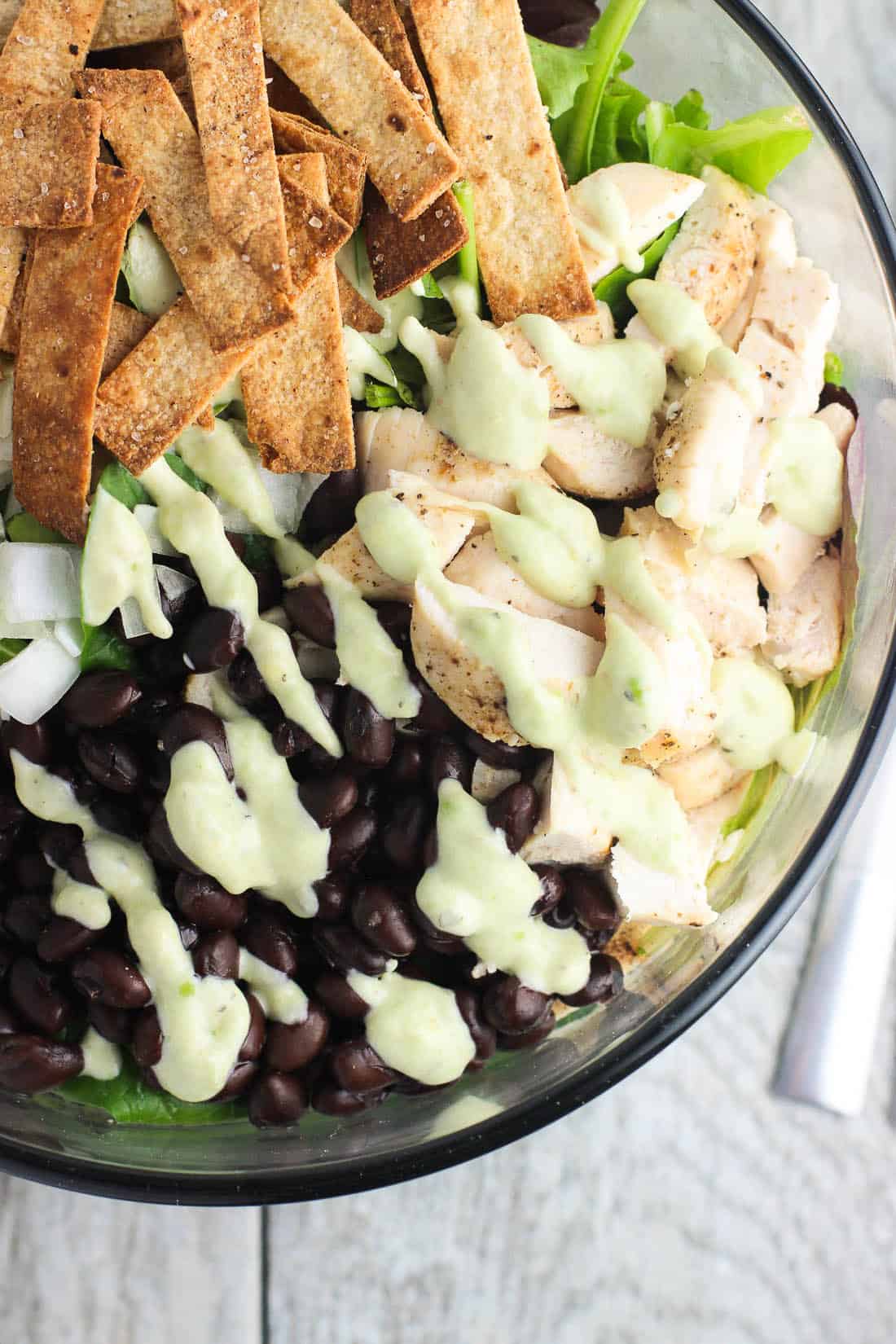 An overhead view of a bowl of salad drizzled with creamy dressing.