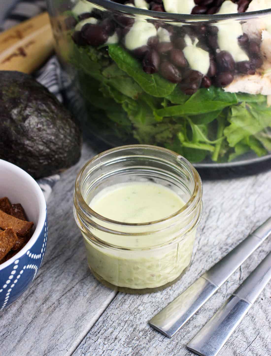 A small bowl of dressing in front of salad ingredients.