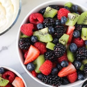 Bowls of fruit salad next to a bowl of whipped cream.