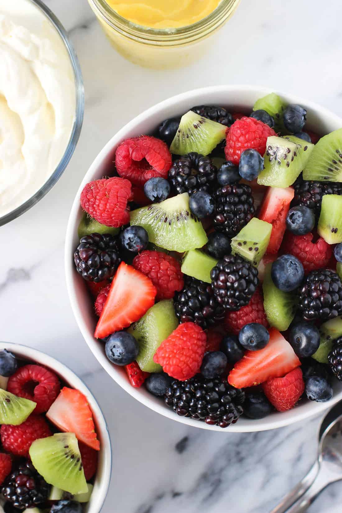 Bowls of fruit salad next to a bowl of whipped cream.