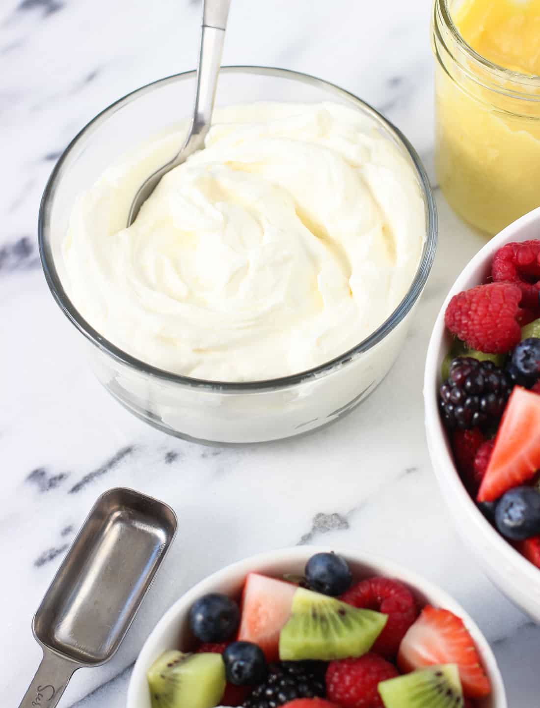 Champagne orange whipped cream in a glass bowl with a spoon next to a jar of curd and a bowl of fruit salad