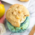 A white chocolate macadamia nut cookie with a bite taken out of it on top of a frosted glass jar of white chocolate chips