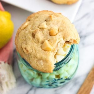 A white chocolate macadamia nut cookie with a bite taken out of it on top of a frosted glass jar of white chocolate chips