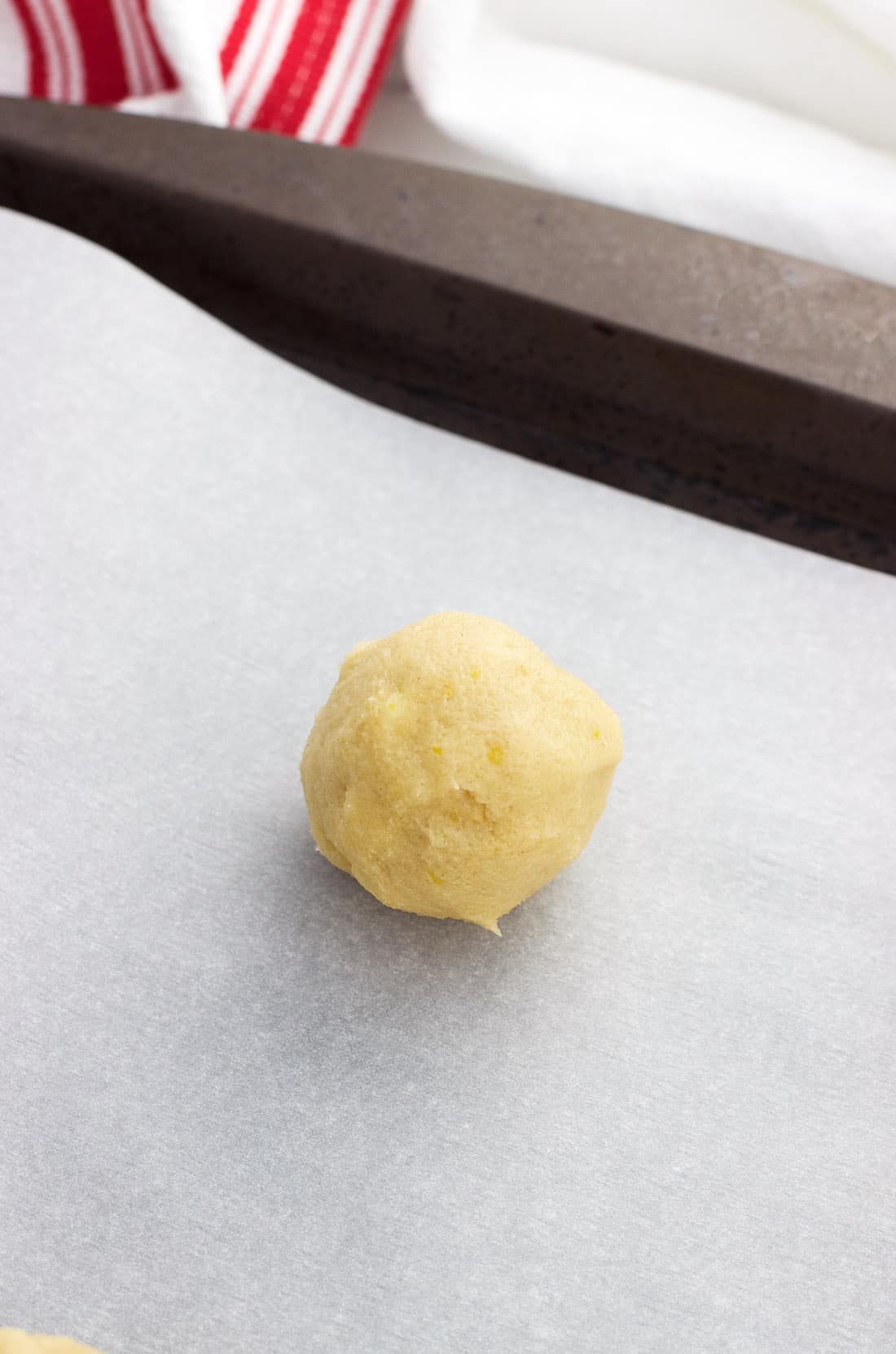 A raw cookie dough ball on a parchment-lined baking sheet