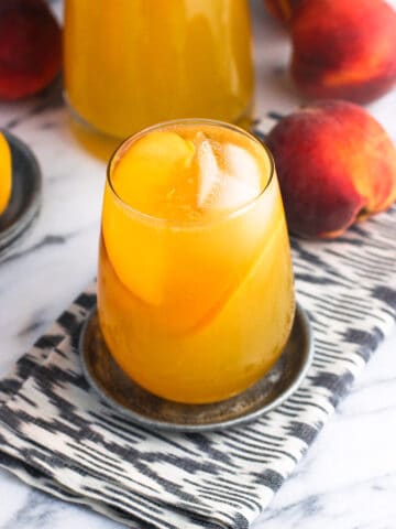 A glass of sangria garnished with ice cubes and peach slices on a metal coaster