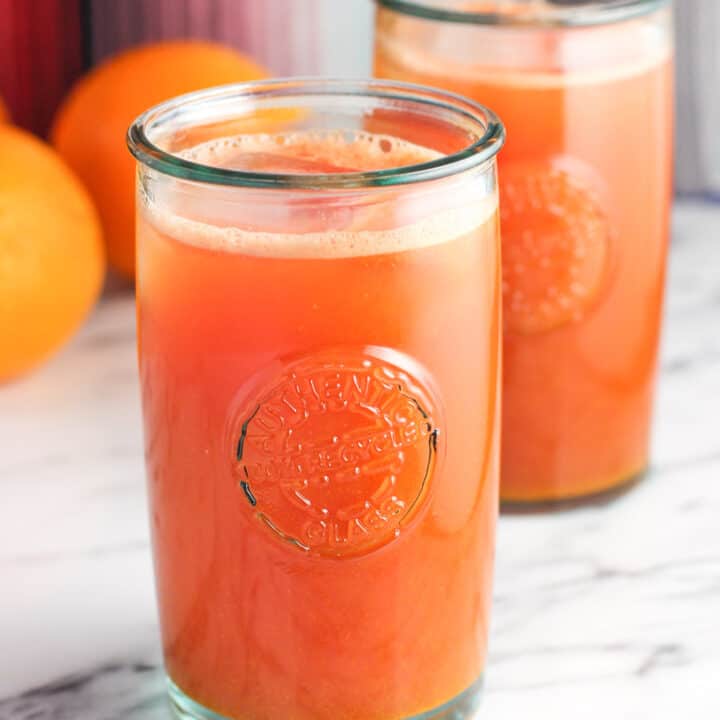 Tall glasses of pressed juice on a table with fresh oranges.