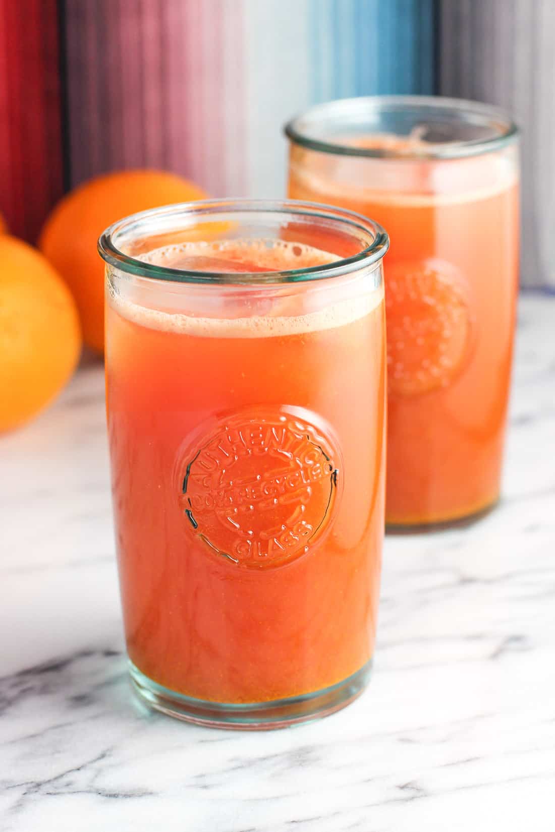 Tall glasses of pressed juice on a table with fresh oranges.