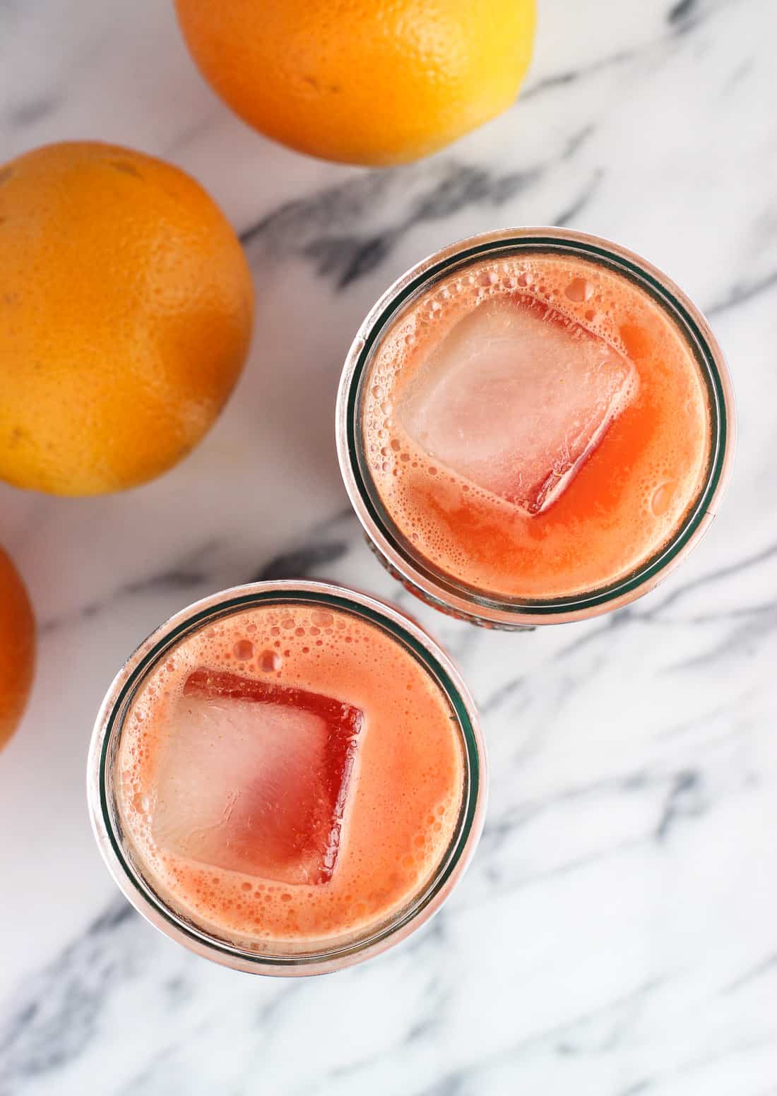 Big ice cubes floating in two glasses of juice.