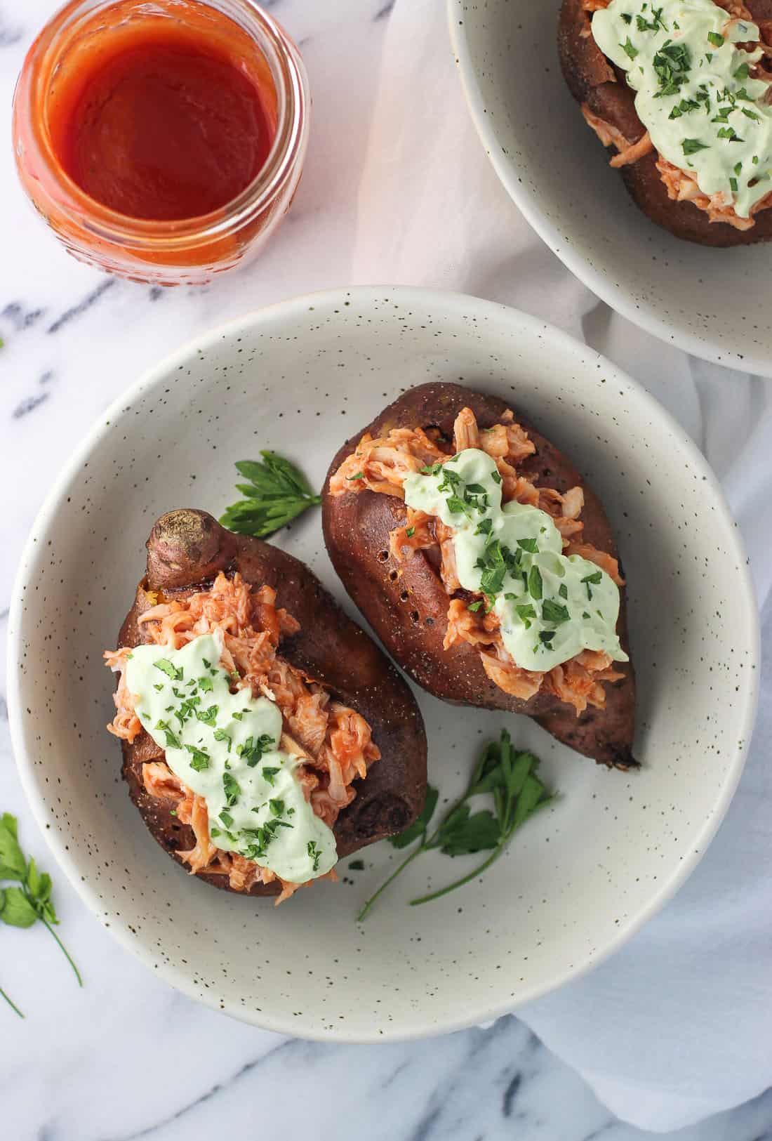 Two BBQ chicken stuffed sweet potatoes in a shallow bowl.