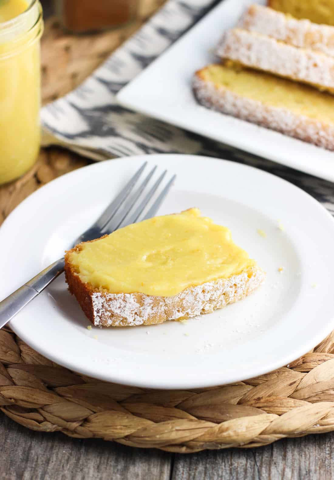 A slice of pound cake topped with citrus curd on a dessert plate with a fork