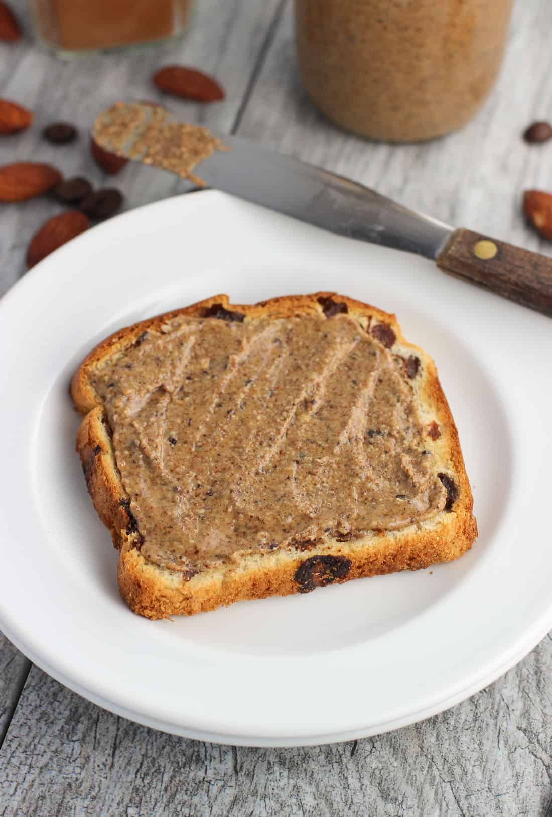 Cinnamon almond butter spread on a slice of cinnamon raisin toast on a small plate