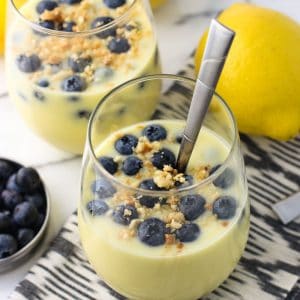 Two servings of pudding in stemless wine glasses, both topped with fresh blueberries and a toasted macadamia nut crumble