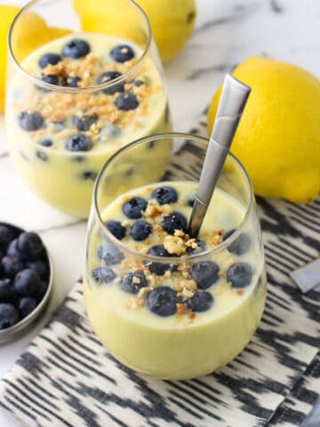 Two servings of pudding in stemless wine glasses, both topped with fresh blueberries and a toasted macadamia nut crumble