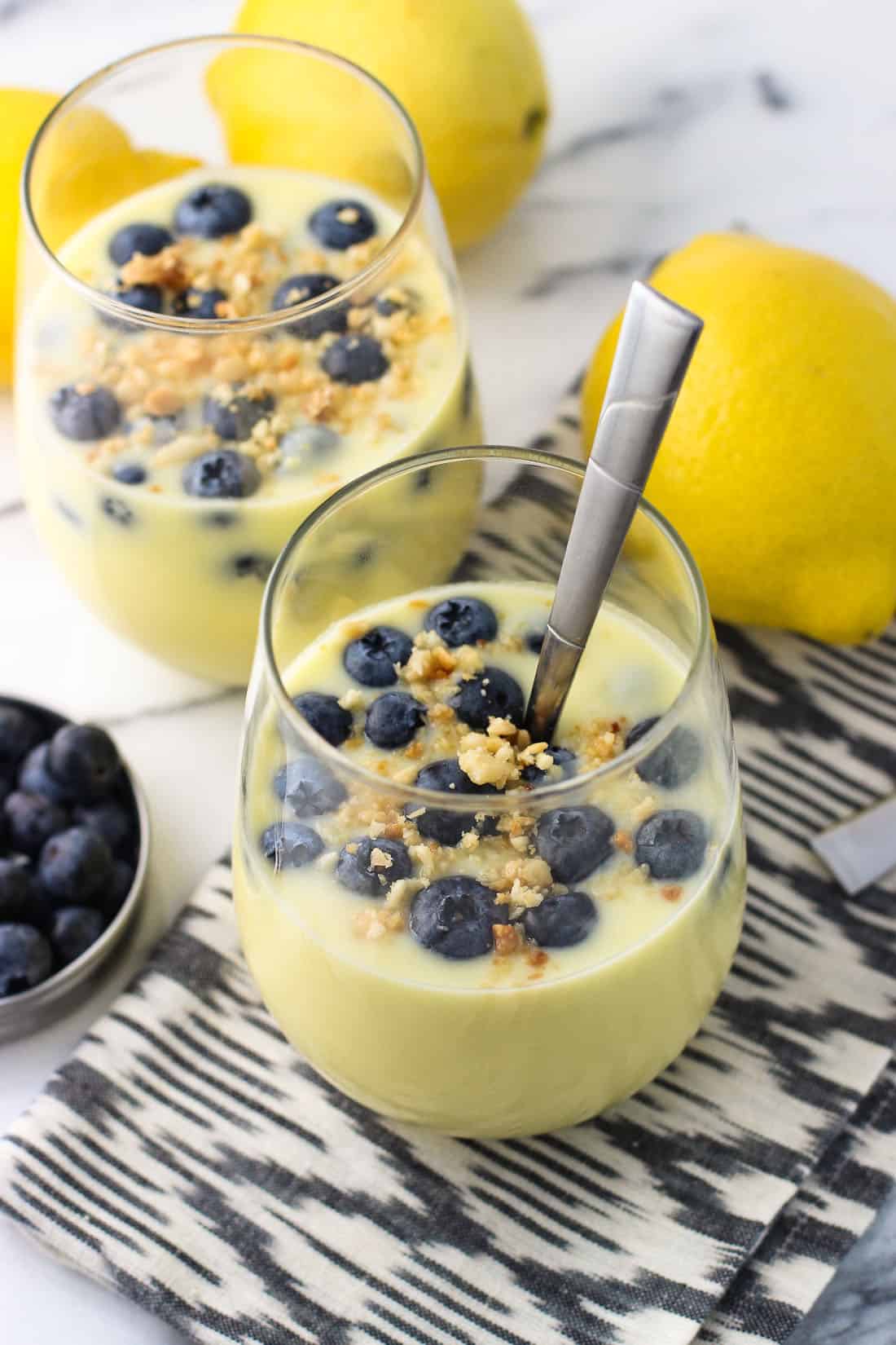 Two servings of pudding in stemless wine glasses, both topped with fresh blueberries and a toasted macadamia nut crumble