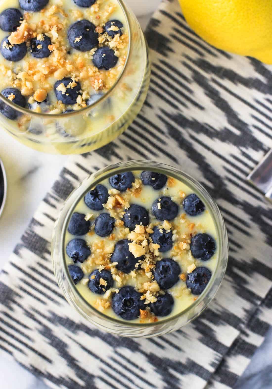 An overhead shot of two glasses filled with lemon pudding, topped with blueberries and nut crumble