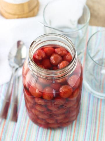 A large glass jar filled with whole cherries and maraschino liquid.