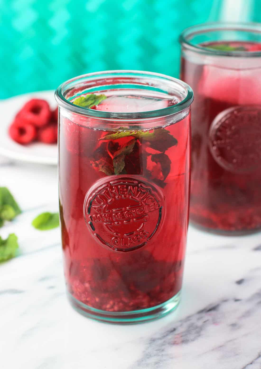 A large glass filled with iced tea garnished with raspberries and fresh mint leaves