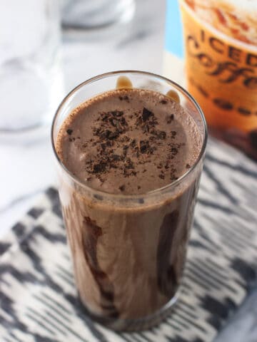 A milkshake in a tall, chocolate syrup lined glass, topped with chocolate shavings.