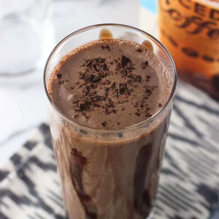 A milkshake in a tall, chocolate syrup lined glass, topped with chocolate shavings.