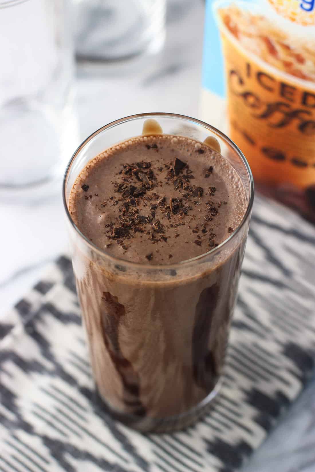 A milkshake in a tall, chocolate syrup lined glass, topped with chocolate shavings. 