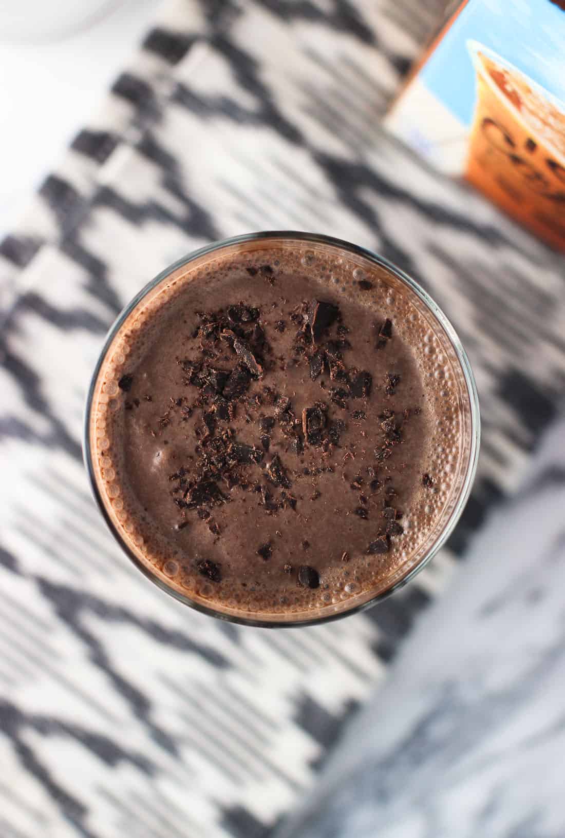 An overhead picture of a chocolate milkshake in a tall glass, garnished with chocolate shavings
