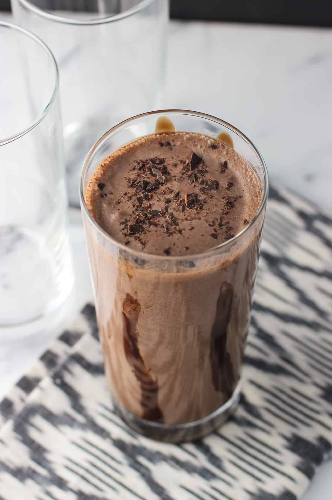 A chocolate milk shake next to two empty glasses