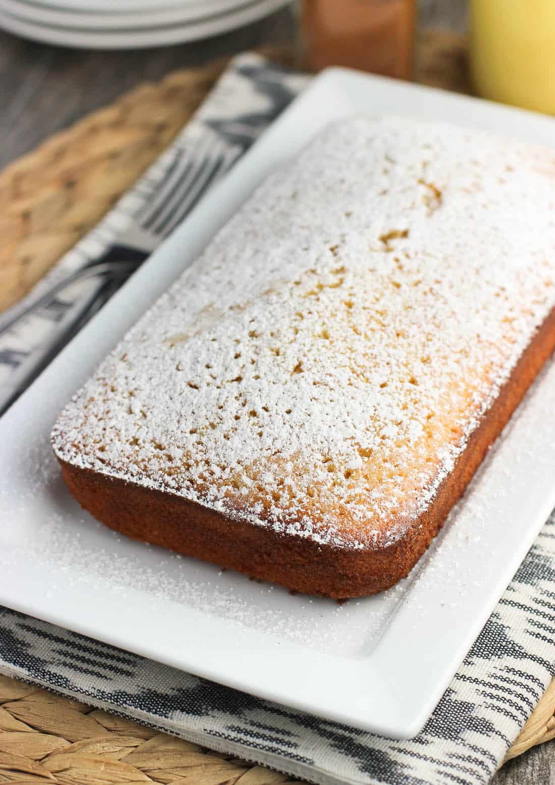 An unsliced loaf of pound cake on a rectangular tray dusted with powdered sugar