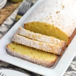 A loaf of pound cake on a tray, dusted with confectioners' sugar and cut into three slices
